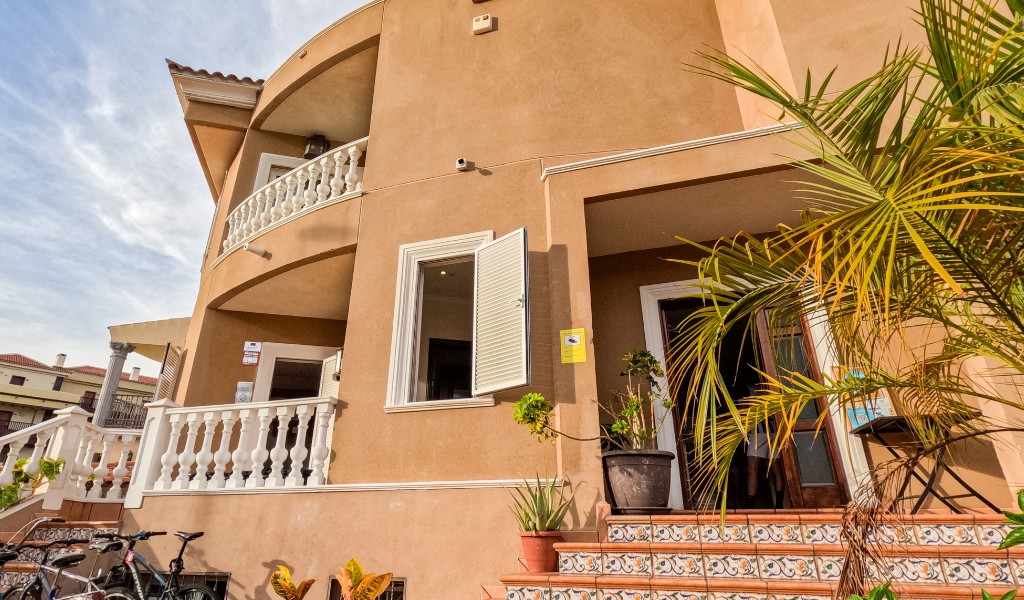 Ingang van een woongebouw met balkon op Tenerife, omringd door planten.
