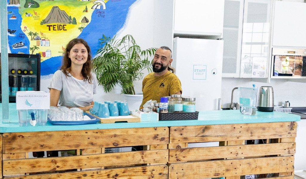 Persoon die achter de bar glimlacht met een kaart van Tenerife op de achtergrond.