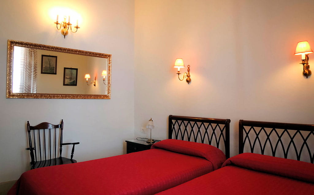 Twee bedden met rode lakens in een verlichte kamer, Puerto de la Cruz.