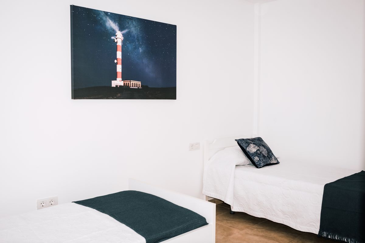 Tweepersoonsbed met witte deklaag en foto van een vuurtoren in een kamer op Tenerife.
