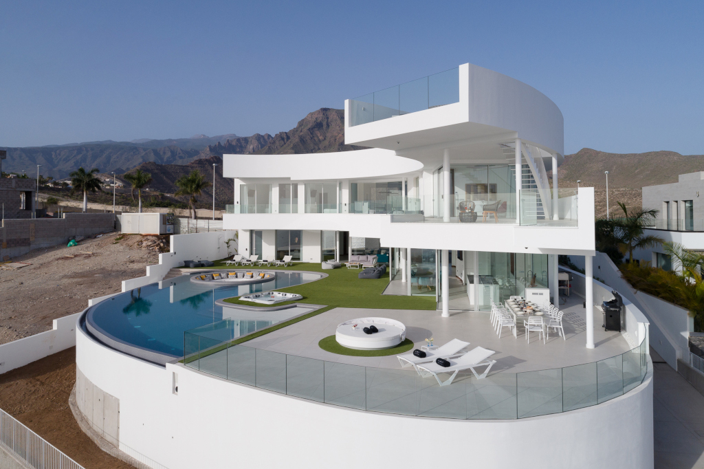 Modern huis met zwembad en terras op Tenerife, omringd door bergen en palmbomen.