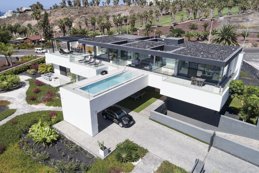 Modern huis met zwembad en auto bij de ingang, een rij palmbomen op de achtergrond op Tenerife.