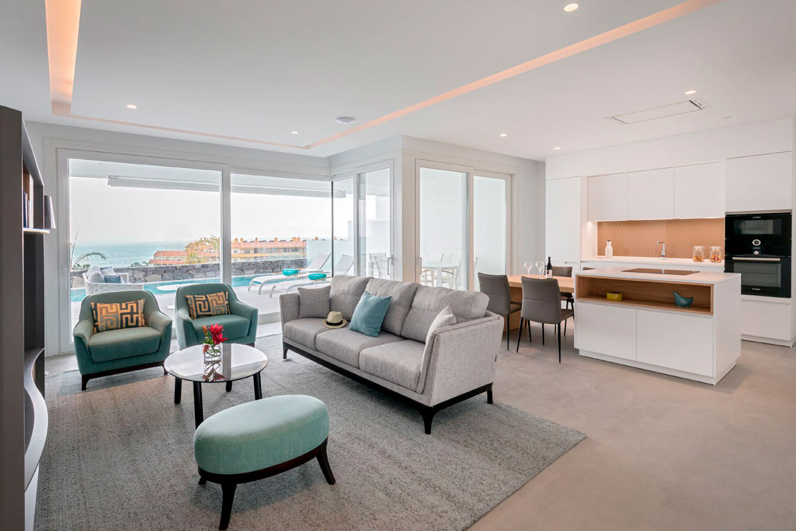 Moderne woonkamer met zeezicht op Tenerife, grijze banken en een geïntegreerde keuken.