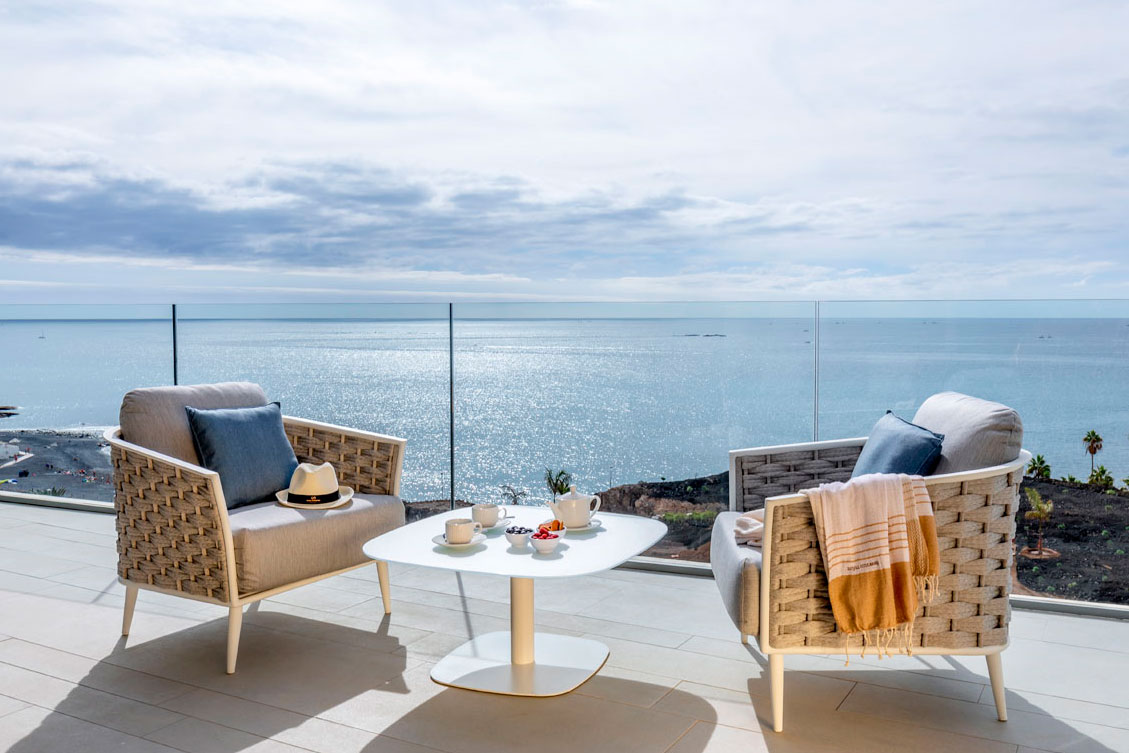 Terras met stoelen en tafel met uitzicht op zee op Tenerife, blauwe achtergrond en een bewolkte lucht.