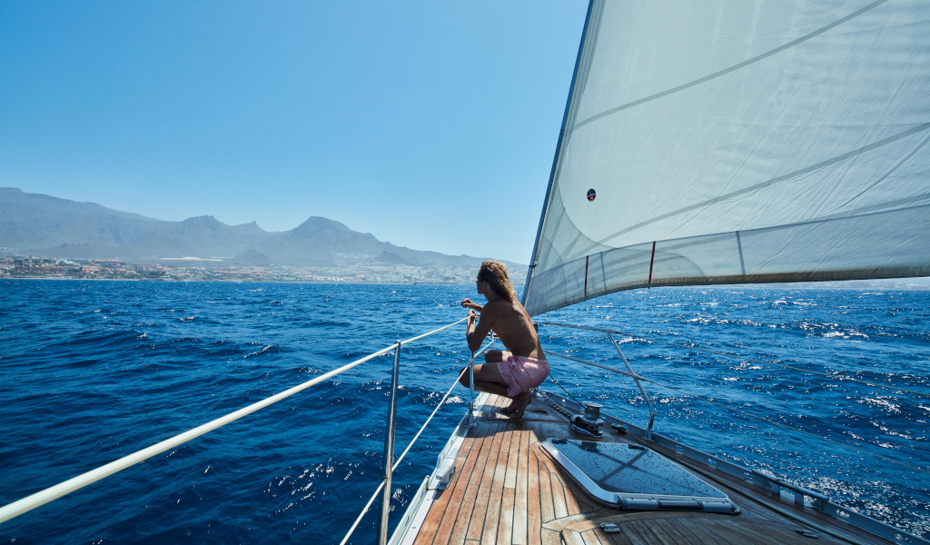 Persoon die met een zeilboot zeilt nabij de kust van Tenerife met bergen op de achtergrond.
