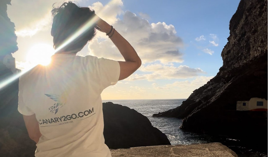 Persoon die CANARY2GO.COM T-shirt draagt voor de zee en een klif op Tenerife.
