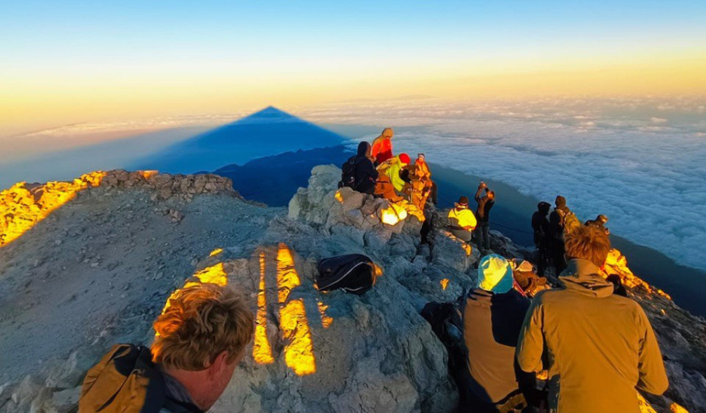 Groep mensen op de top van de berg Teide bij zonsopgang, kijkend naar de schaduw die op de wolken viel.