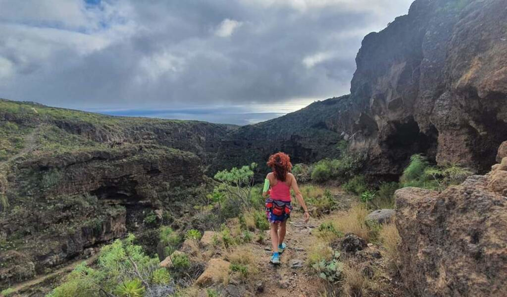 Persoon die over een rotsachtig pad in een ravijn op Tenerife loopt onder een bewolkte lucht.