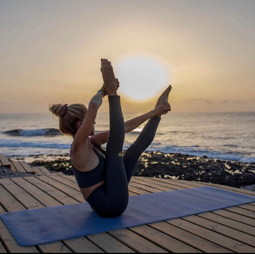 Persoon die yoga beoefent bij zonsondergang op een platform aan zee op Tenerife.