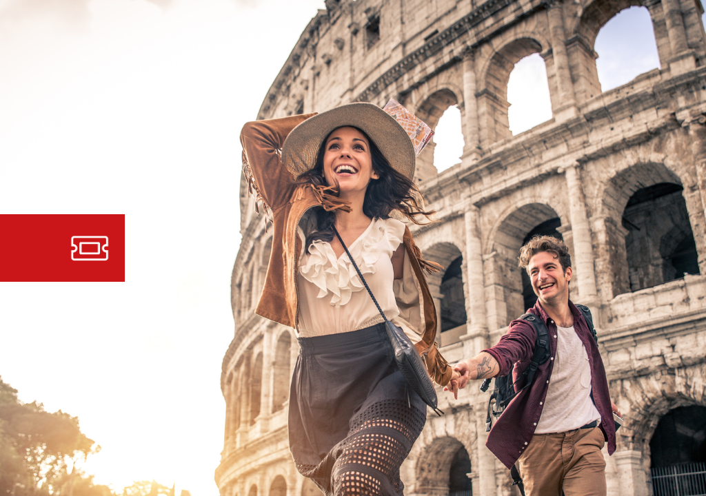 Een paar glimlachende toeristen die bij zonsondergang voor het Colosseum in Rome rennen, met rugzakken en casual kleding aan.