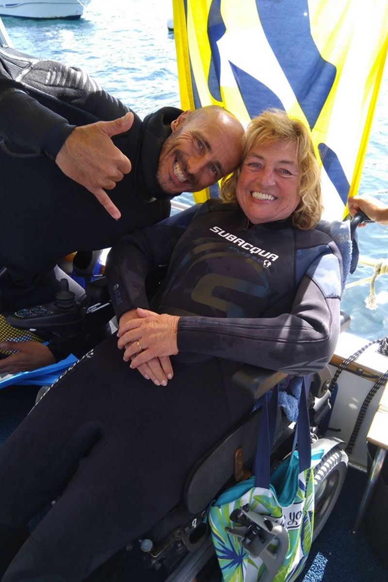 Mensen in lachende duikpakken in een rolstoel bij zee op Tenerife.