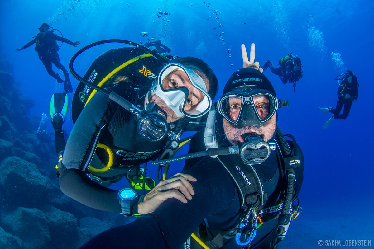 Duikers die onder water glimlachen op Tenerife met anderen op de achtergrond.