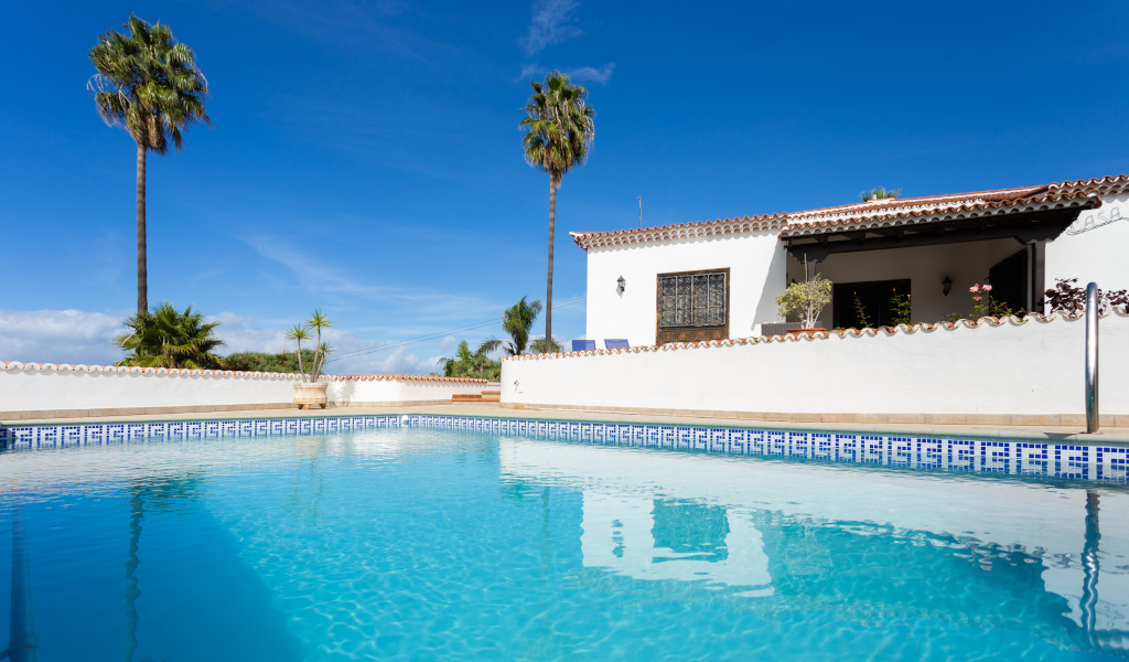 Zwembad en huis met palmbomen op Tenerife onder een blauwe lucht.