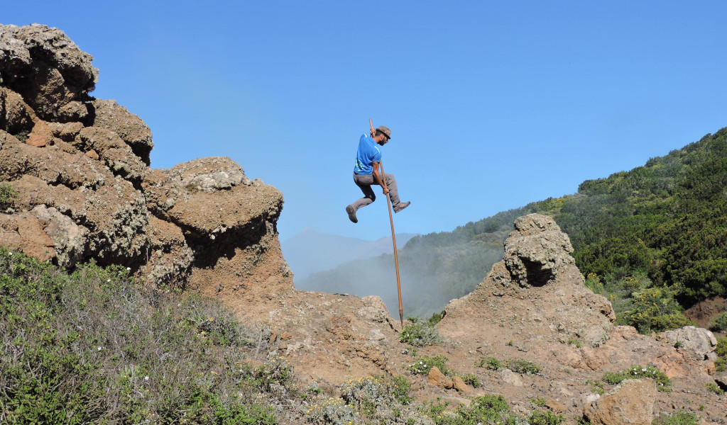 Persoon die een knots gebruikt om tussen rotsen te springen in een landschap van Tenerife.