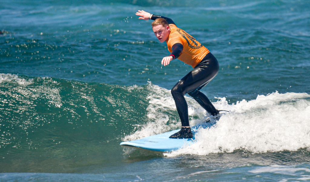 Persoon die op een golf surft op Tenerife, in een oranje wetsuit gekleed.