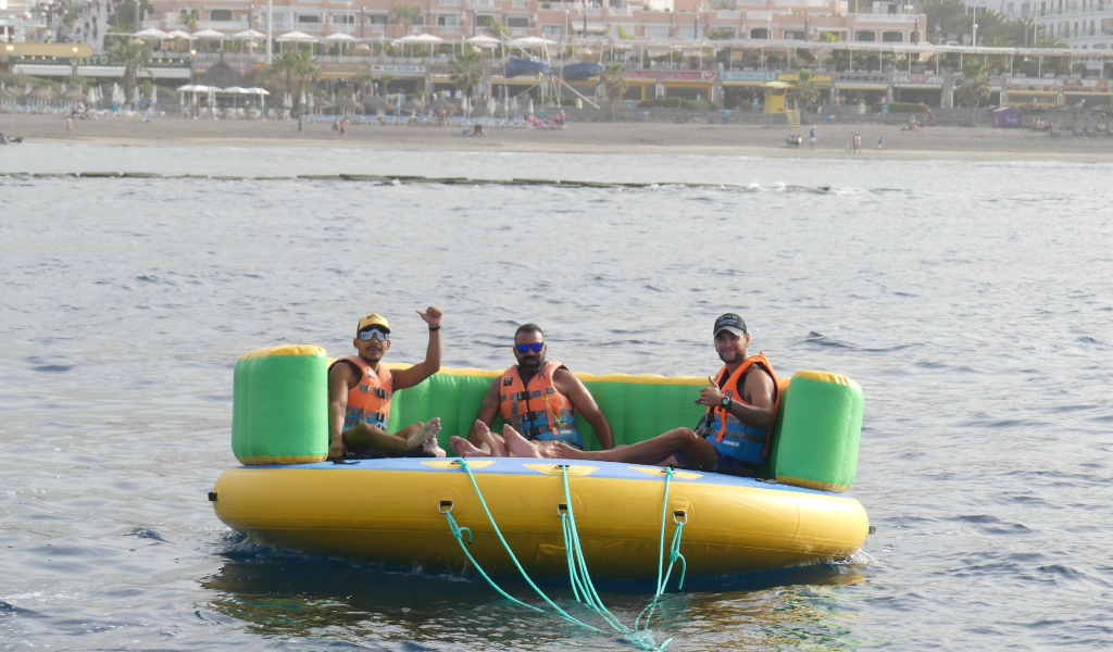 Drie mensen op een opblaasplatform in zee, Playa de las Americas op de achtergrond, Tenerife.