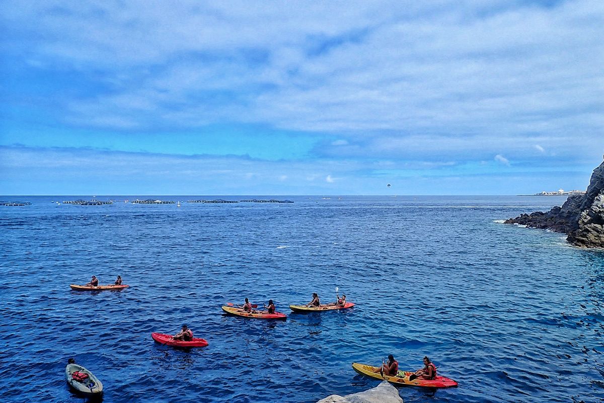 Verschillende mensen kajakken aan de kust van Tenerife onder deels bewolkte lucht.