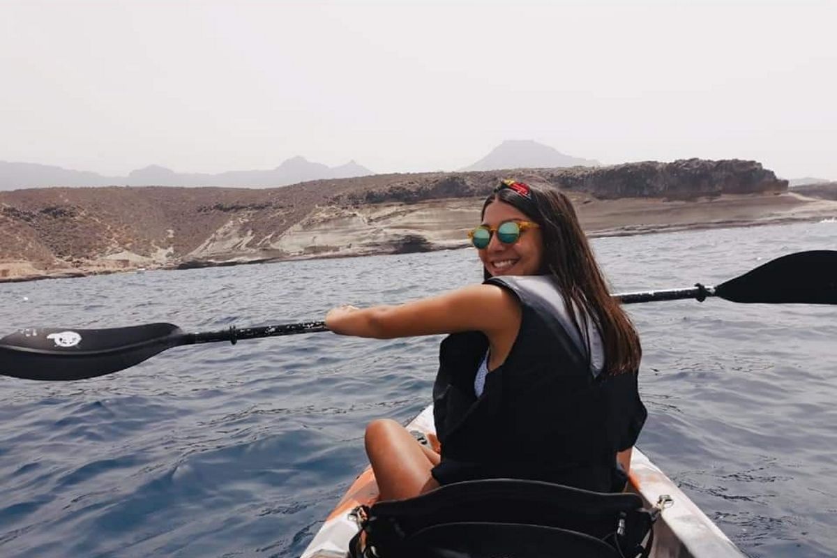 Persoon die met een kajak peddelt in het water van Tenerife, met een bergachtig landschap op de achtergrond.