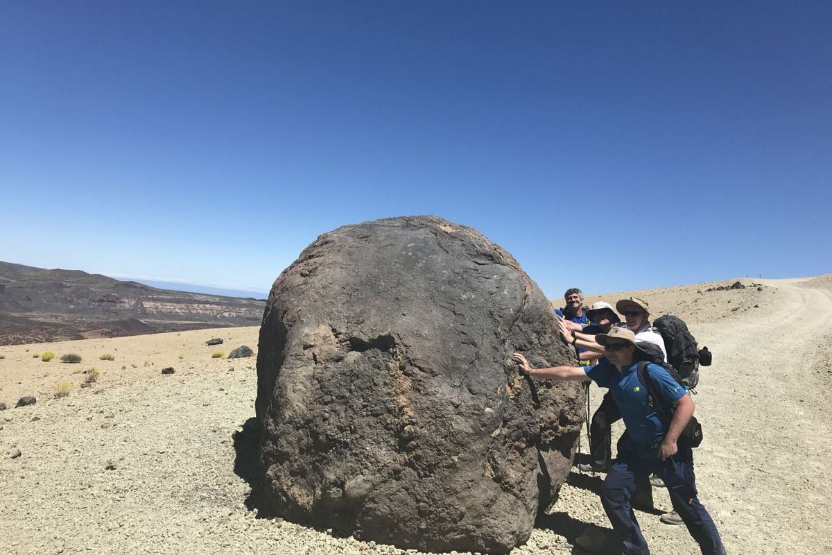 Mensen die een grote rots in het vulkanische landschap van Nationaal Park Teide, Tenerife, duwen.