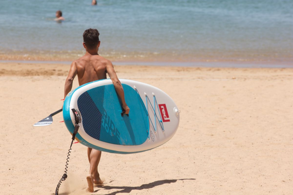 Iemand die met een paddleboard loopt op het strand van Tenerife.