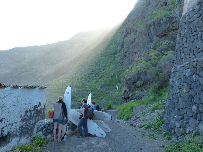 Mensen met surfplanken die over een pad op Tenerife lopen, omringd door bergen.
