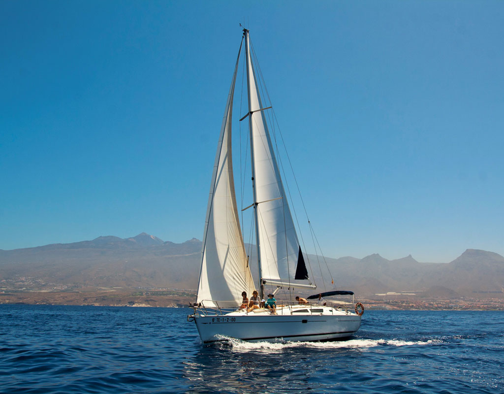 Zeilboot die voor de kust van Tenerife zeilt met bergen op de achtergrond.