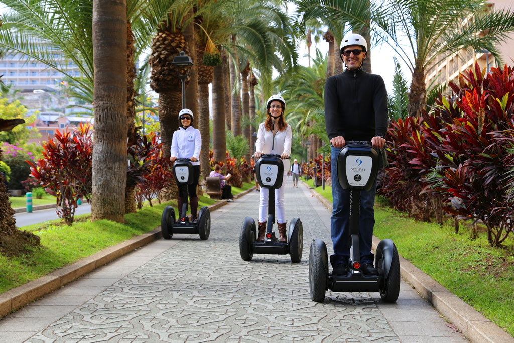 Drie mensen op segways rijden langs een met palmen omzoomde laan op Tenerife.