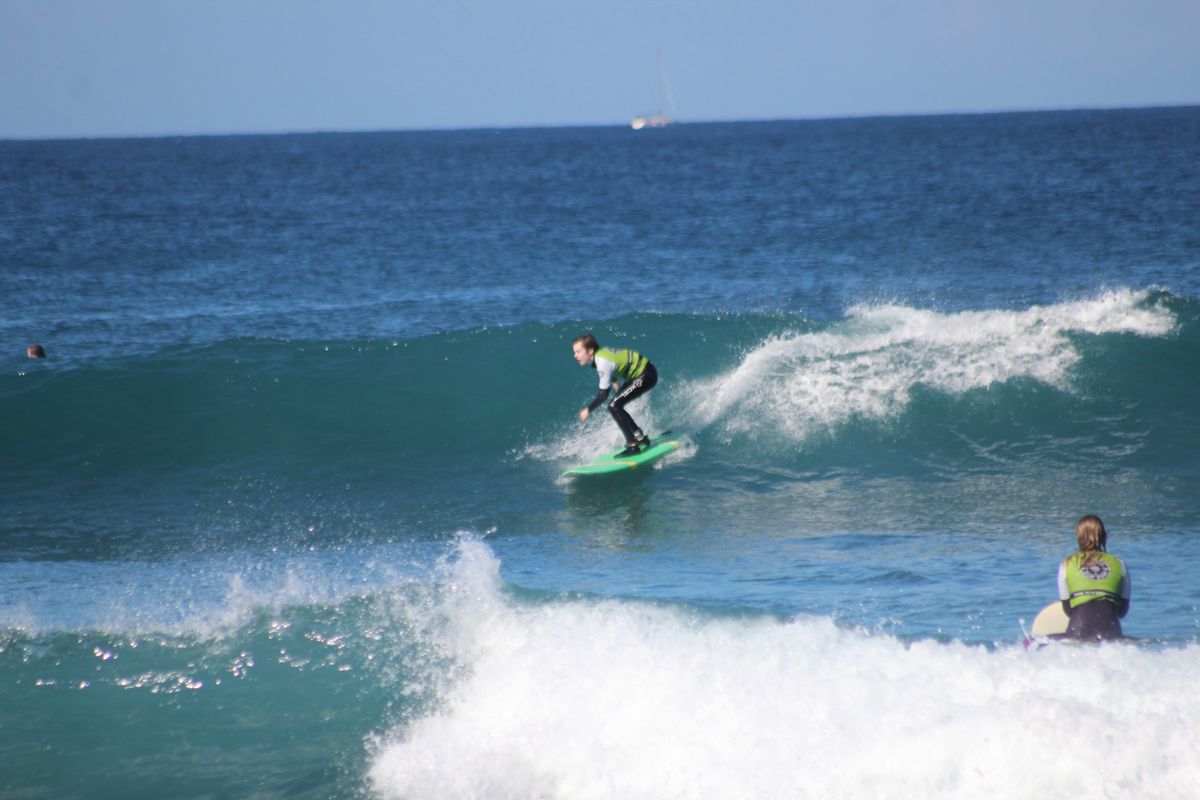 Surfer surft op een golf op Tenerife, met iemand anders die vanuit het water toekijkt.
