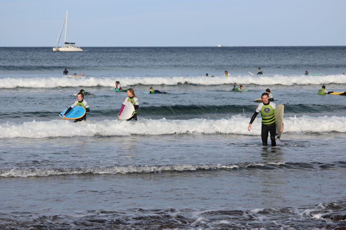 Surfers met boards in Playa de Las Américas, Tenerife, met een zeilboot op de achtergrond.