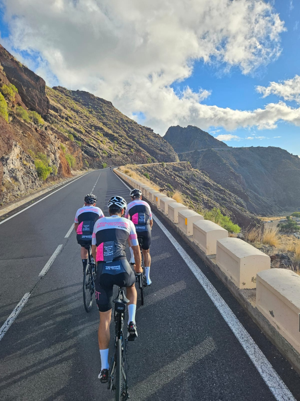 Fietsers die een bergachtige weg beklimmen op Tenerife onder deels bewolkte luchten.