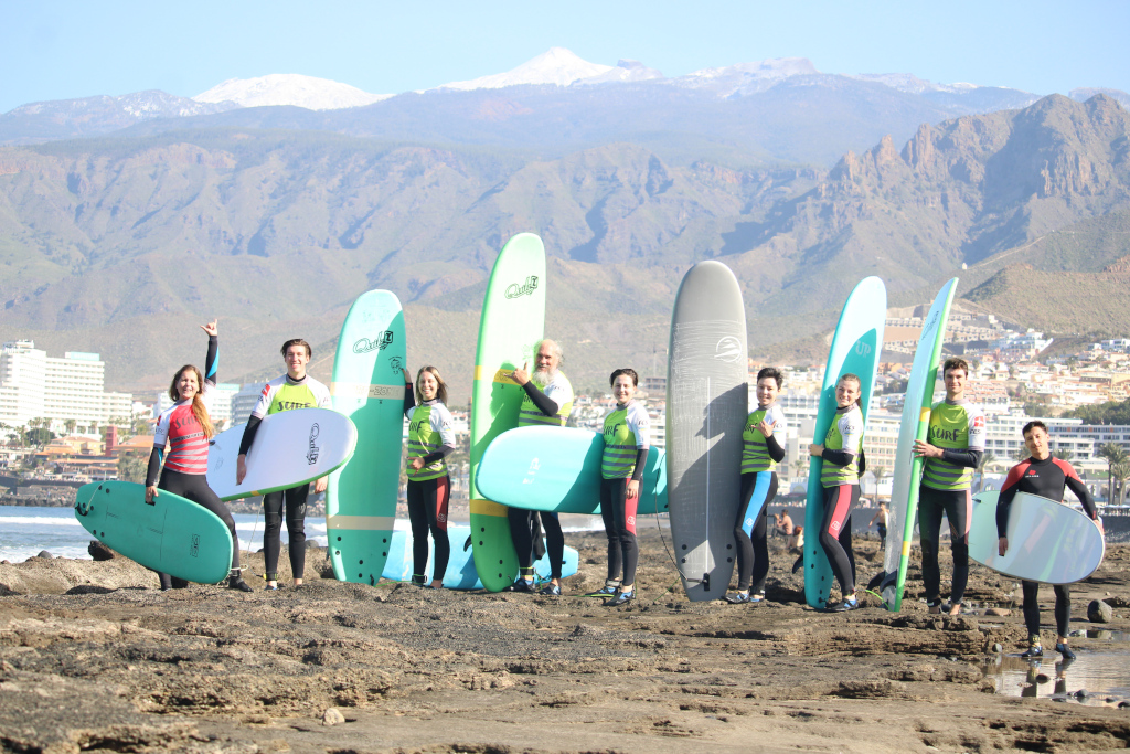 Groep surfers met planken op het strand van Tenerife, bergen op de achtergrond.