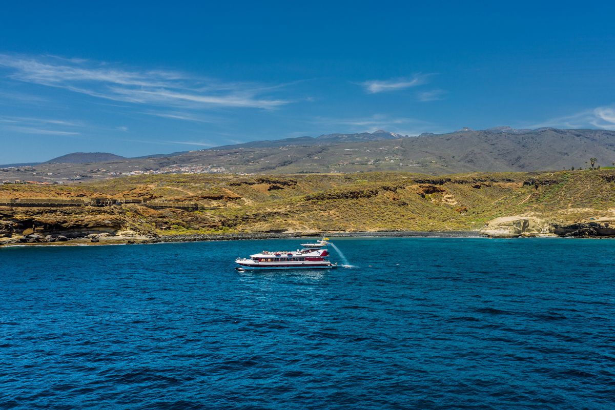Boot die dicht langs de kust zeilt met bergen op de achtergrond op Tenerife.