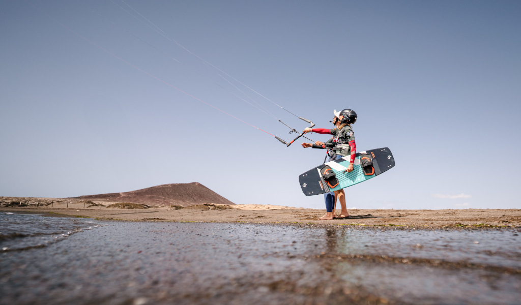 Persoon die kitesurfen beoefent in Playa El Médano, Tenerife, met een heuvel op de achtergrond.