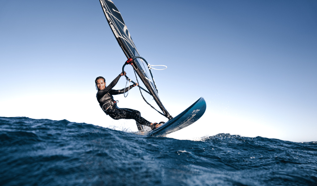 Persoon die windsurft in zee bij Tenerife onder een heldere lucht.