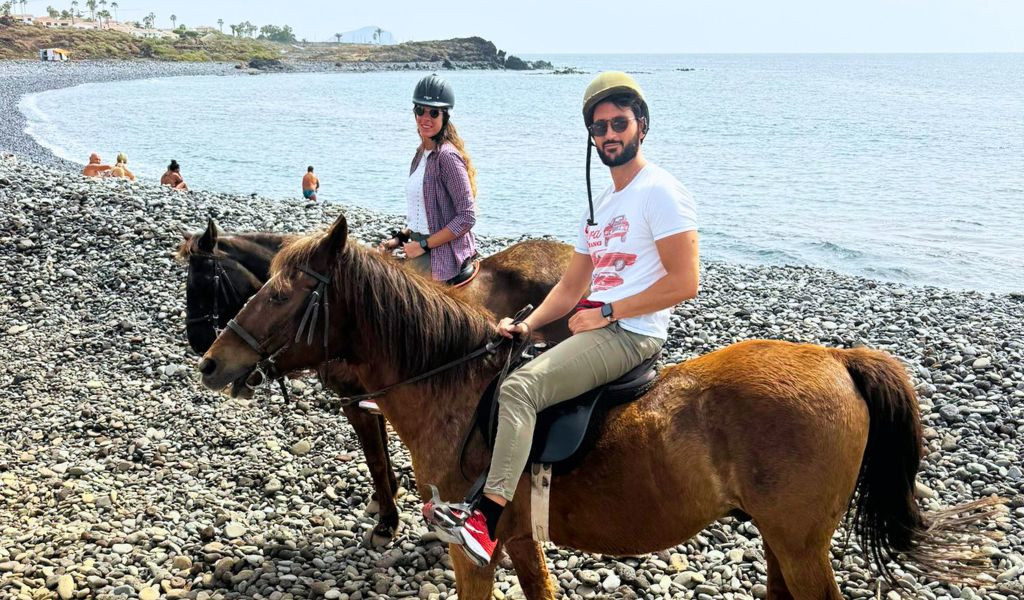 Mensen die te paard rijden op het kiezelstrand van Tenerife, met de zee op de achtergrond.