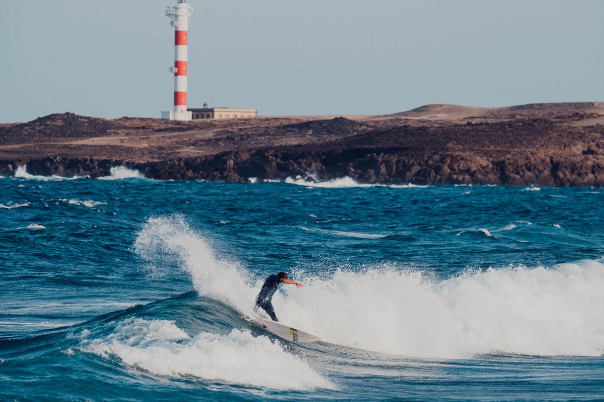 Surfer die op een golf rijdt voor de vuurtoren in Punta de Hidalgo, Tenerife.