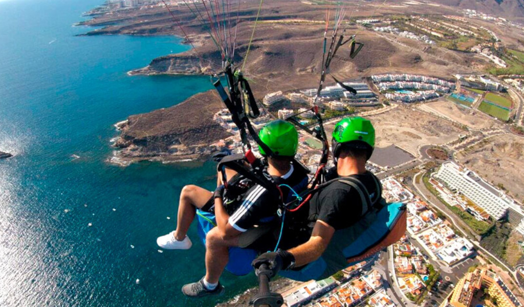 Mensen paragliden boven de kust van Tenerife met uitzicht vanuit de lucht op zee en gebouwen.