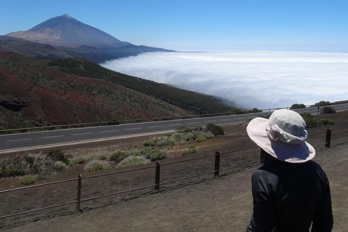Iemand met een hoed die naar de Teide en de zee van wolken op Tenerife kijkt.