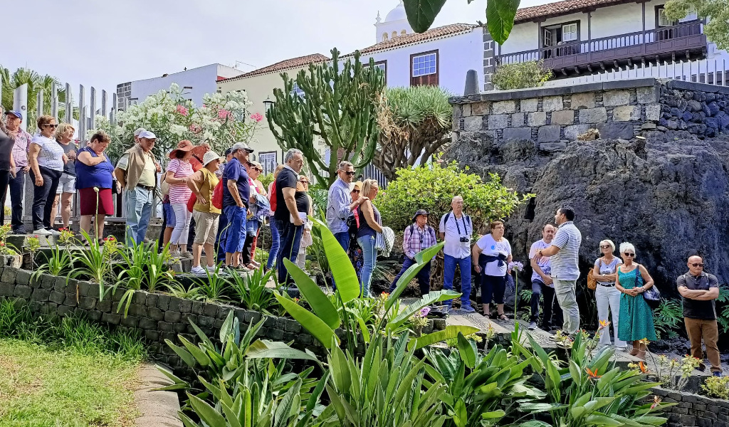 Groep mensen die door een tuin wandelen op een plek op Tenerife, omringd door planten en lokale architectuur.