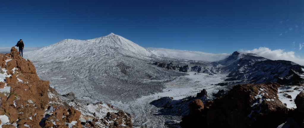 Besneeuwd landschap van de berg Teide op Tenerife met een wandelaar bovenop een rots.