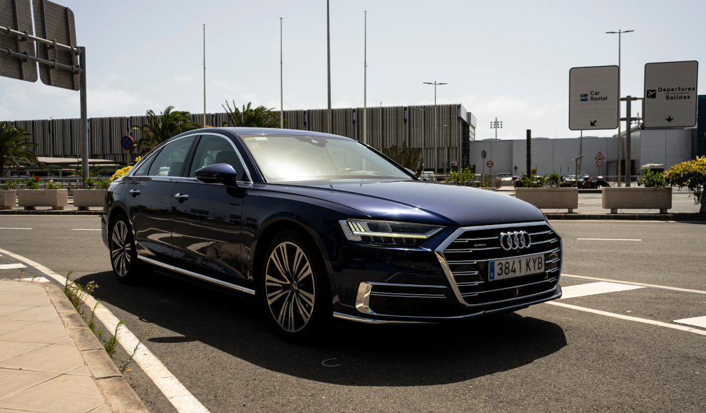 Blauwe auto geparkeerd voor de luchthaven Tenerife Zuid, met een autoverhuurbord.