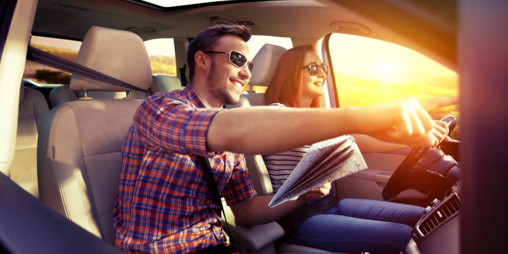 Glimlachend stel in een auto met kaart op Tenerife tijdens zonsondergang.