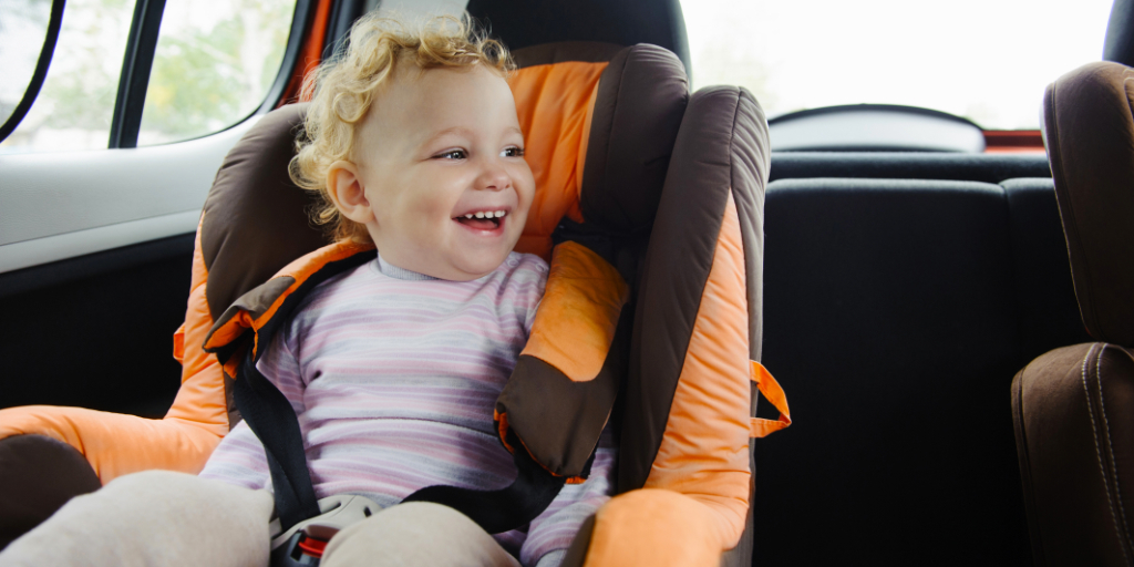 Kind dat lacht in een autostoeltje in een auto.