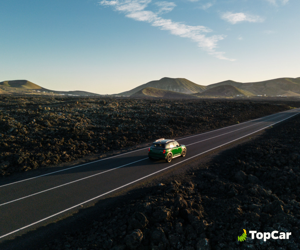 Groene auto rijdt over de weg tussen vulkanische landschappen op Tenerife. TopCar-logo.