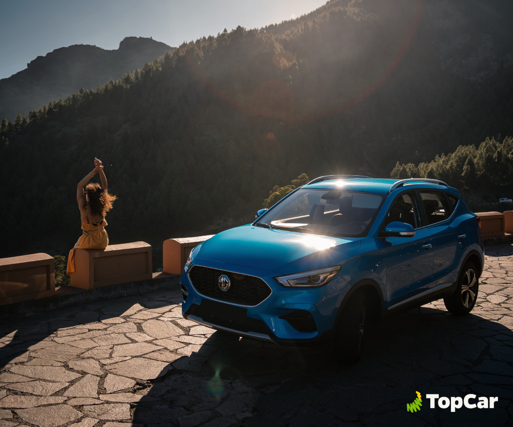 Blauwe auto voor bergen op Tenerife, vrouw die op een muur zit in de zon.