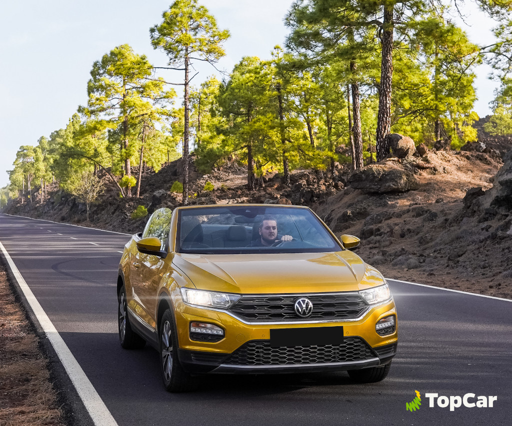Gele auto op de weg omringd door dennenbomen op Tenerife. TopCar-logo.