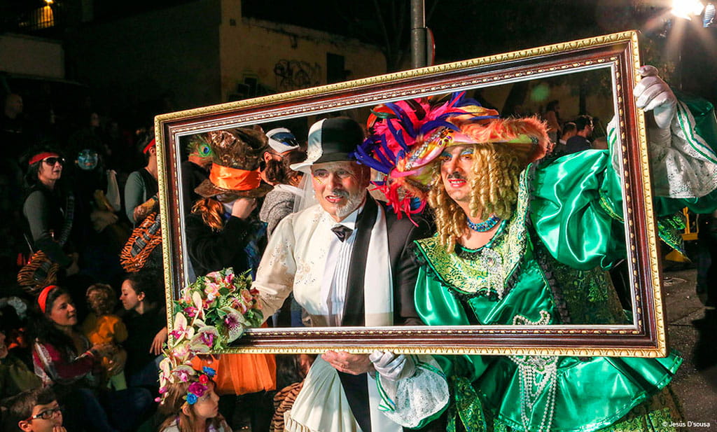 Mensen in kleurrijke kostuums poseren achter een lijst op het carnaval van Tenerife.