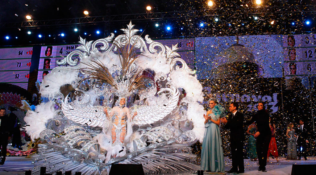 Persoon in een sierlijk kostuum op het Carnaval van Tenerife, omringd door confetti en lichtjes.