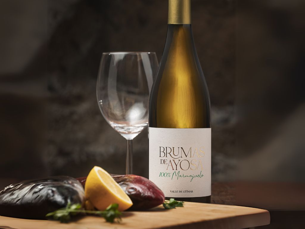 Fles Brumas de Ayosa-wijn met leeg glas, citroen en aubergines. Tekst: 100% Marmajuelo. Güímarvallei.