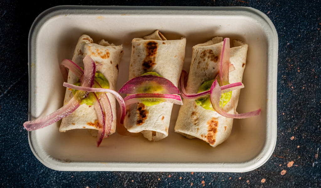 Drie burrito's met rode ui en salsa verde op een rechthoekig bord op Tenerife.
